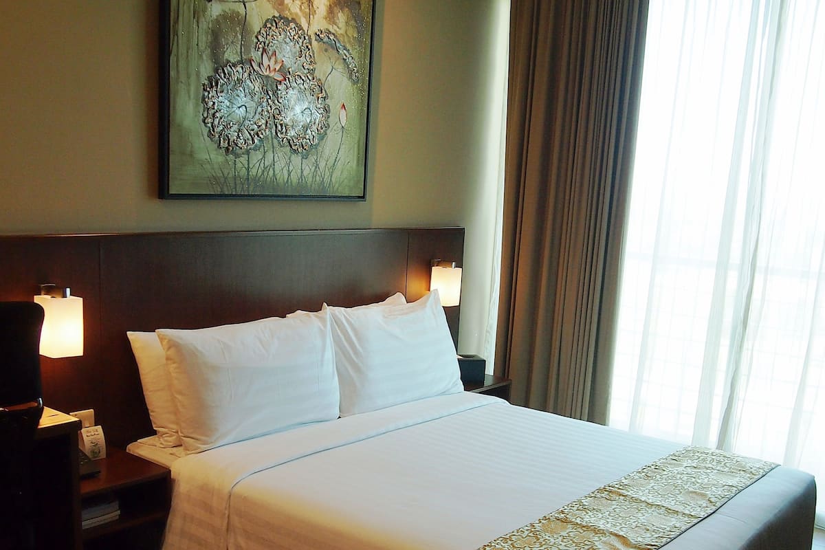 A hotel room with a large bed, a headboard, a nightstand, a lamp, and a painting on the wall.