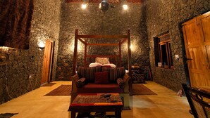 A room with a four-poster bed, stone walls, a wooden door, and a small table with a rug. - Kurulu Estate (Rakwana)