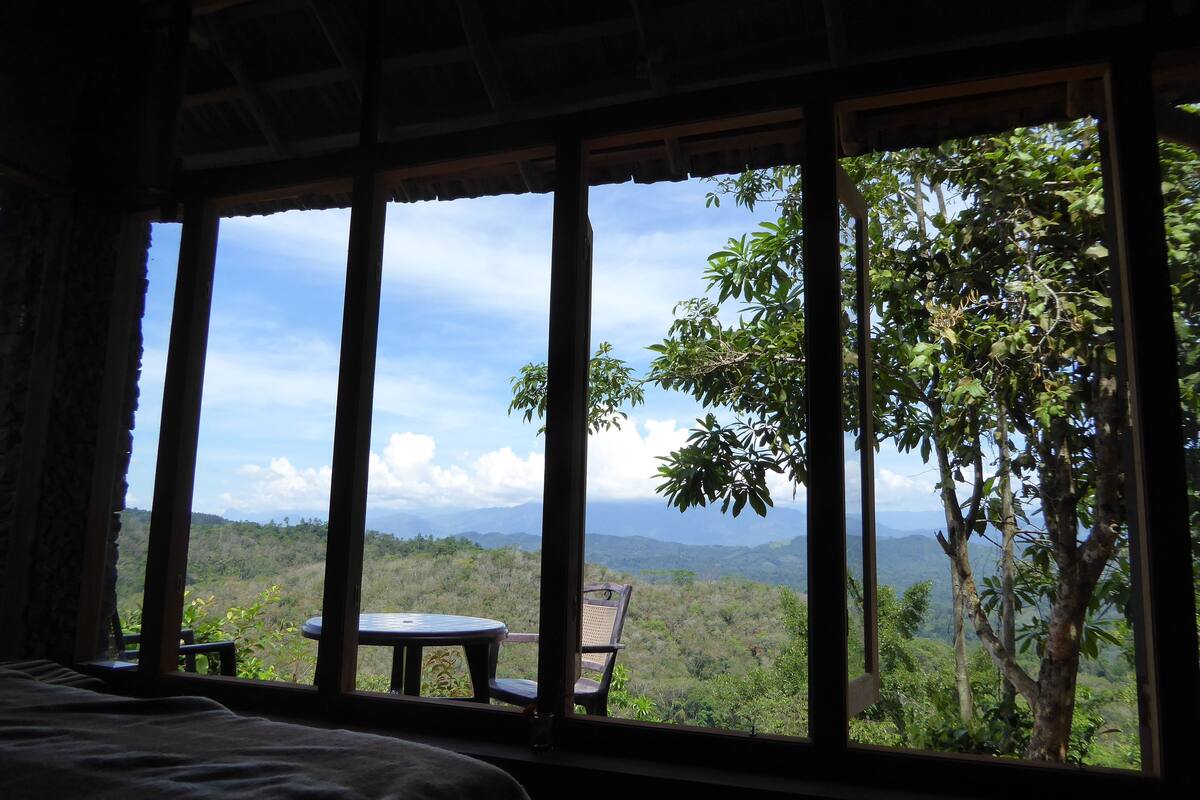 A room with a large window, a bed, and a small table.