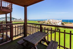 A wooden deck with a picnic table and benches overlooking a coastal area with buildings and a clear sky.