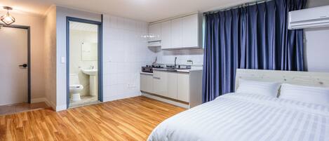 Una moderna camera d'albergo con pavimento in legno, un letto con biancheria bianca, angolo cottura e bagno con WC e lavandino.
