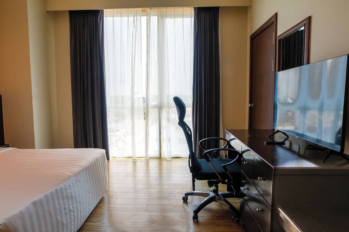 A hotel room with a bed, a desk with a chair, a television, and a sliding glass door to the outside.