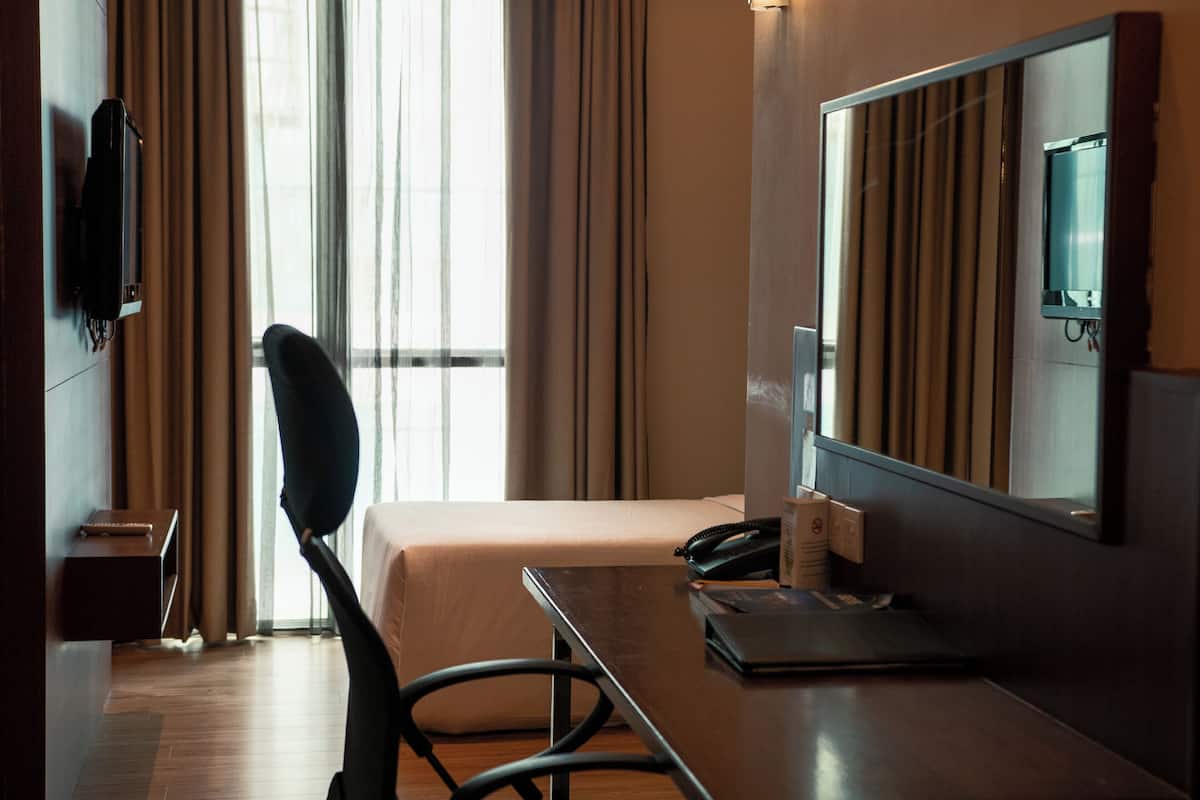 A hotel room with a bed, a desk, a chair, a television, and a window with curtains.