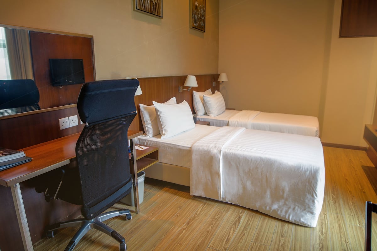 A hotel room with a desk, two beds, a chair, and a TV.