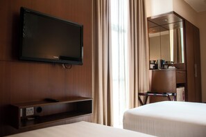Una habitación de hotel con televisión en la pared, una cama, una mesita de noche y un espejo.