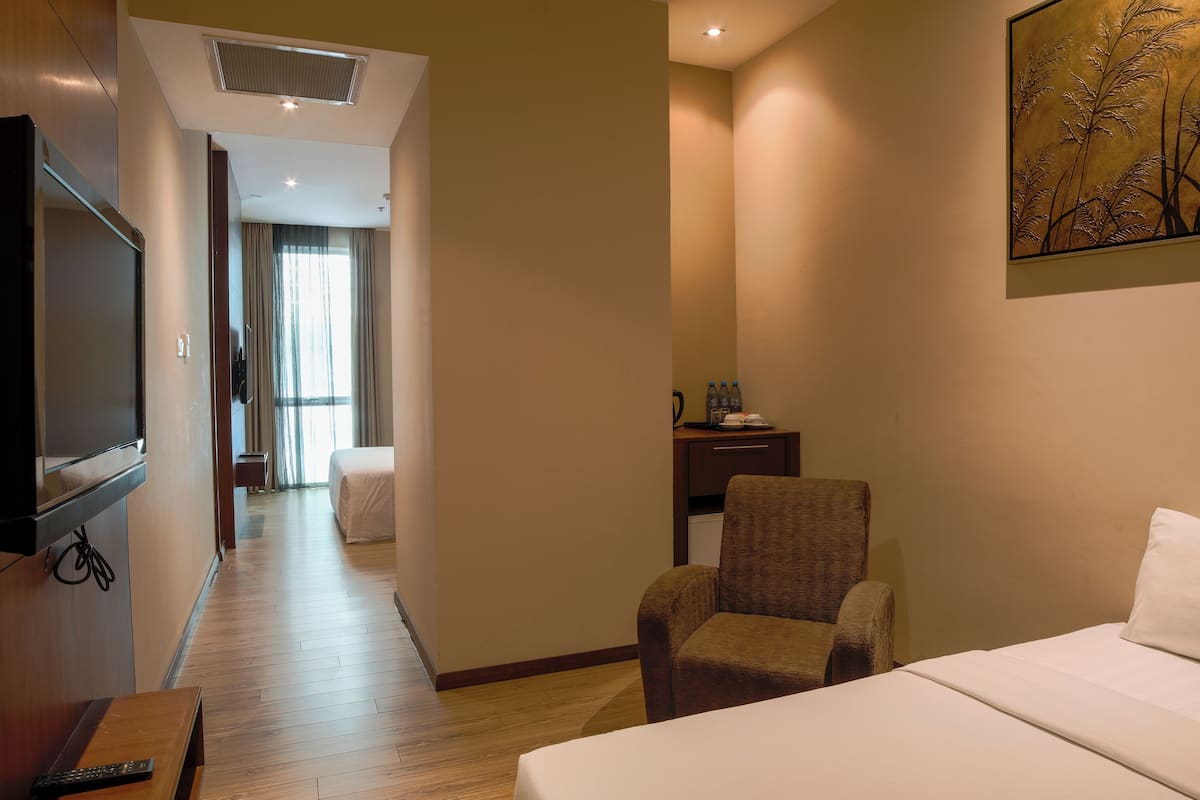 A hotel room with a bed, a chair, a desk with a lamp, a television, and a painting on the wall.