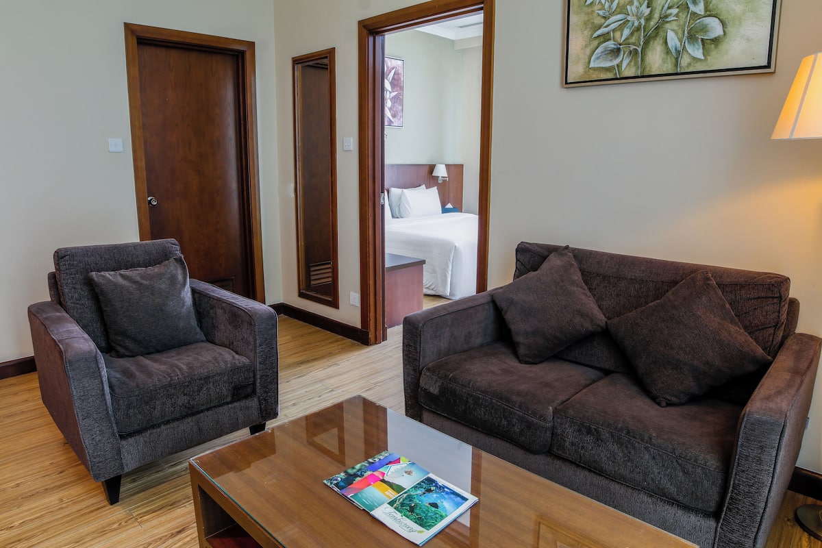 A hotel room with two armchairs, a wooden coffee table, and a bed with white bedding.
