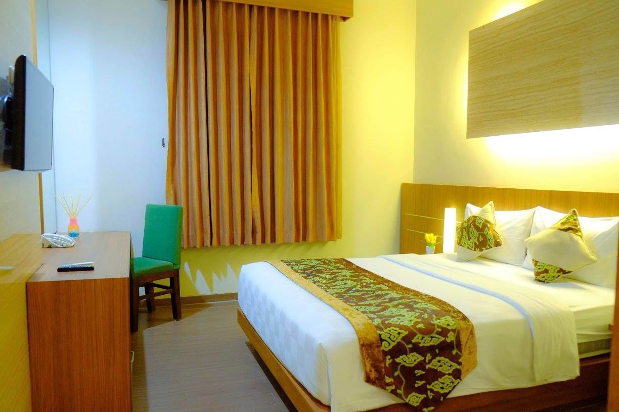 Ein Hotelzimmer mit Bett, Schreibtisch, Stuhl, Fernseher und einem fensterbepflanzten Fenster.