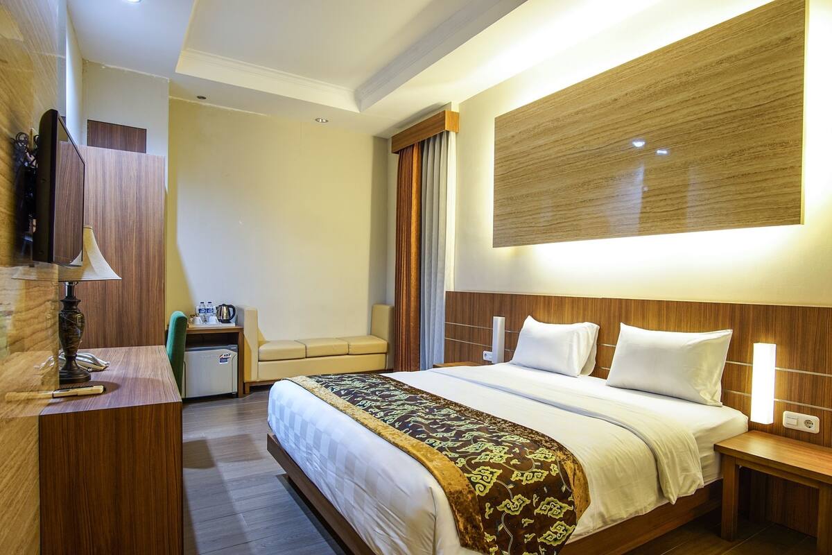 A hotel room with a large bed, bedside tables, a desk, and a mirror.
