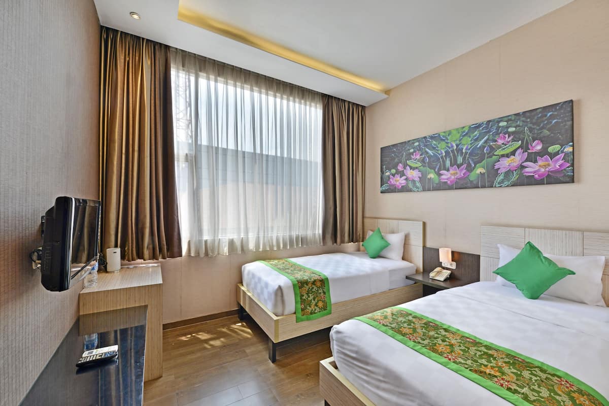A hotel room with two beds, a TV, a desk, and a painting of flowers.