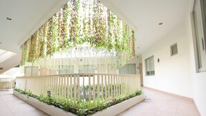 A spacious indoor area with a central garden, white walls, and a tiled floor. - Legreen Suite Penjernihan (Jakarta)