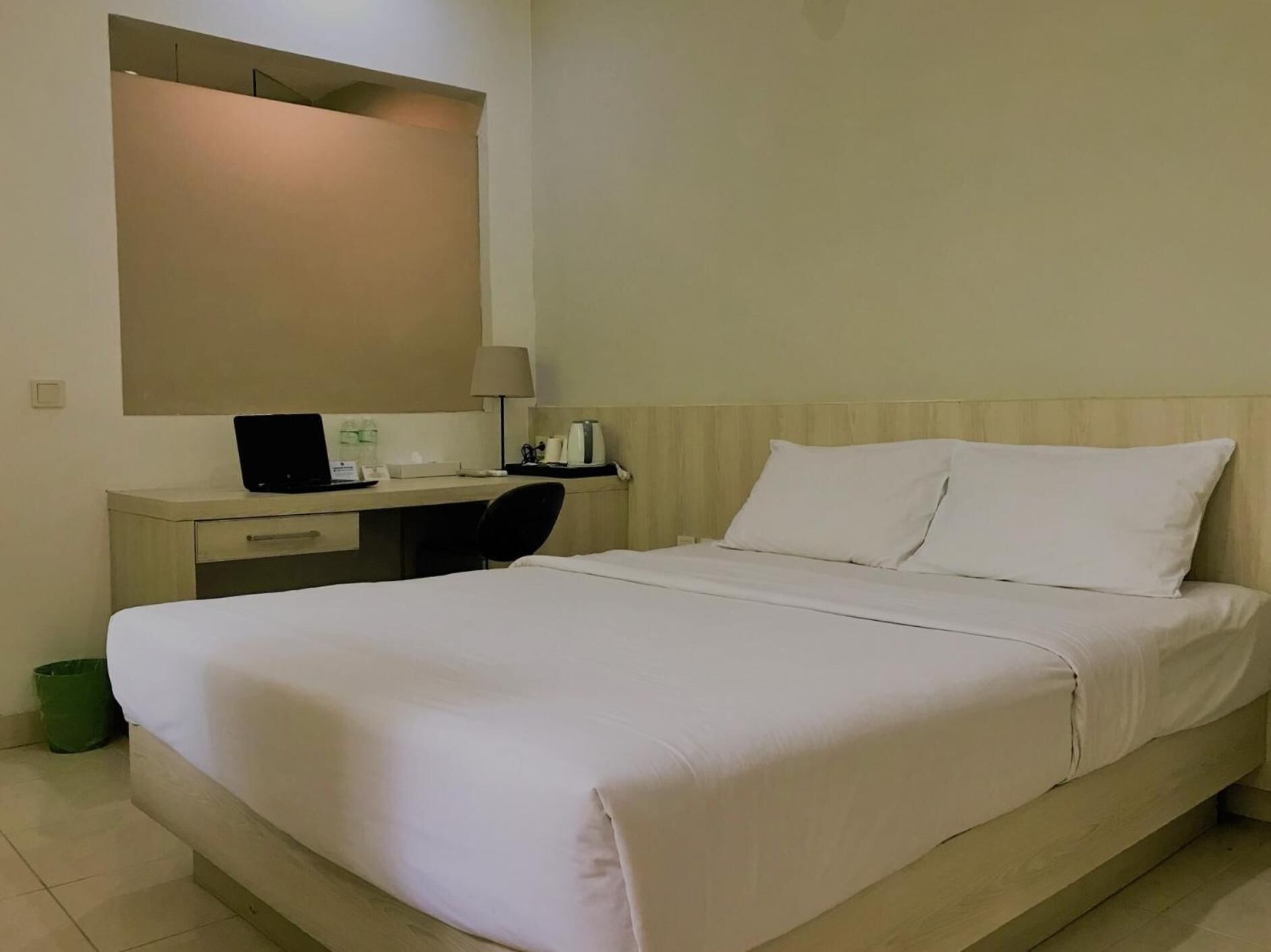 A hotel room with a bed, a desk, a chair, a lamp, and a trash bin.