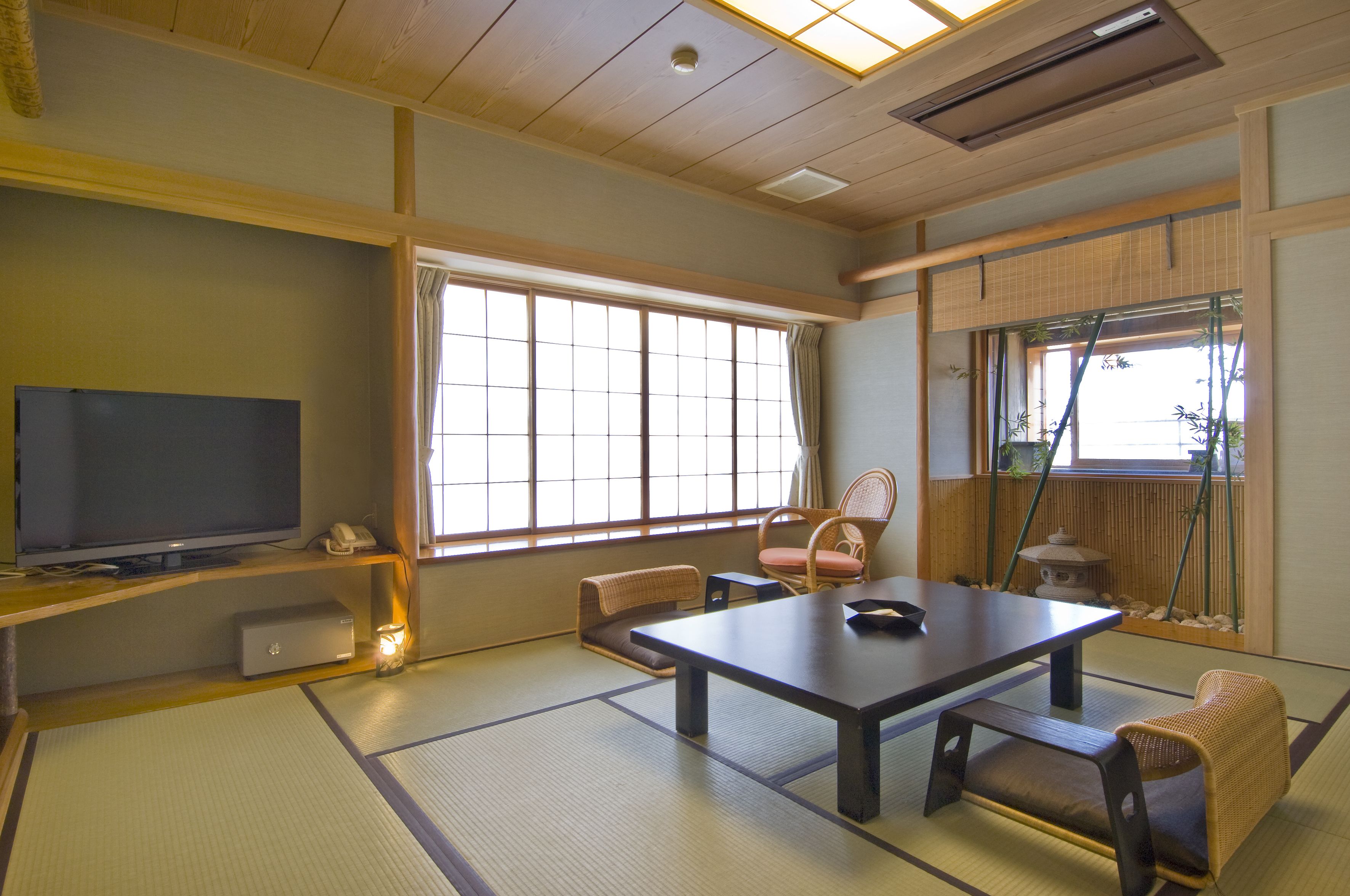 A traditional Japanese room with tatami flooring, a low table, and a television on a shelf.
