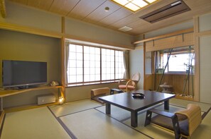 A traditional Japanese room with tatami flooring, a low table, and a television on a shelf. - Moriaki Ryokan (Shibukawa)