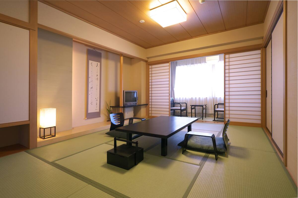 A traditional Japanese room with tatami flooring, a low table, chairs, a television, and a sliding door.