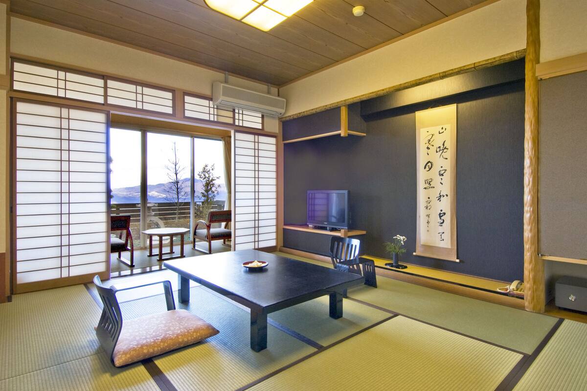 A traditional Japanese room with tatami flooring, a low table, chairs, a television, and a shoji screen.