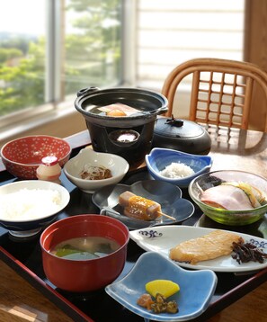 Un montaje tradicional de comida japonesa con diversos platos en una bandeja, incluyendo una tetera, cuencos de arroz y otros alimentos.