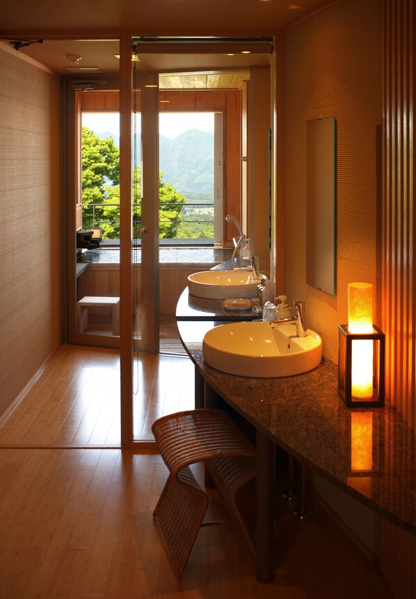 Un baño moderno con dos lavamanos, un banco y vistas a montañas a través de una puerta de cristal.