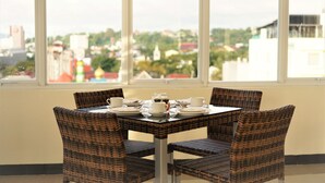 Una mesa de comedor con cuatro sillas de mimbre, dispuesta para cuatro personas, con vistas a un paisaje urbano a través de amplios ventanales.