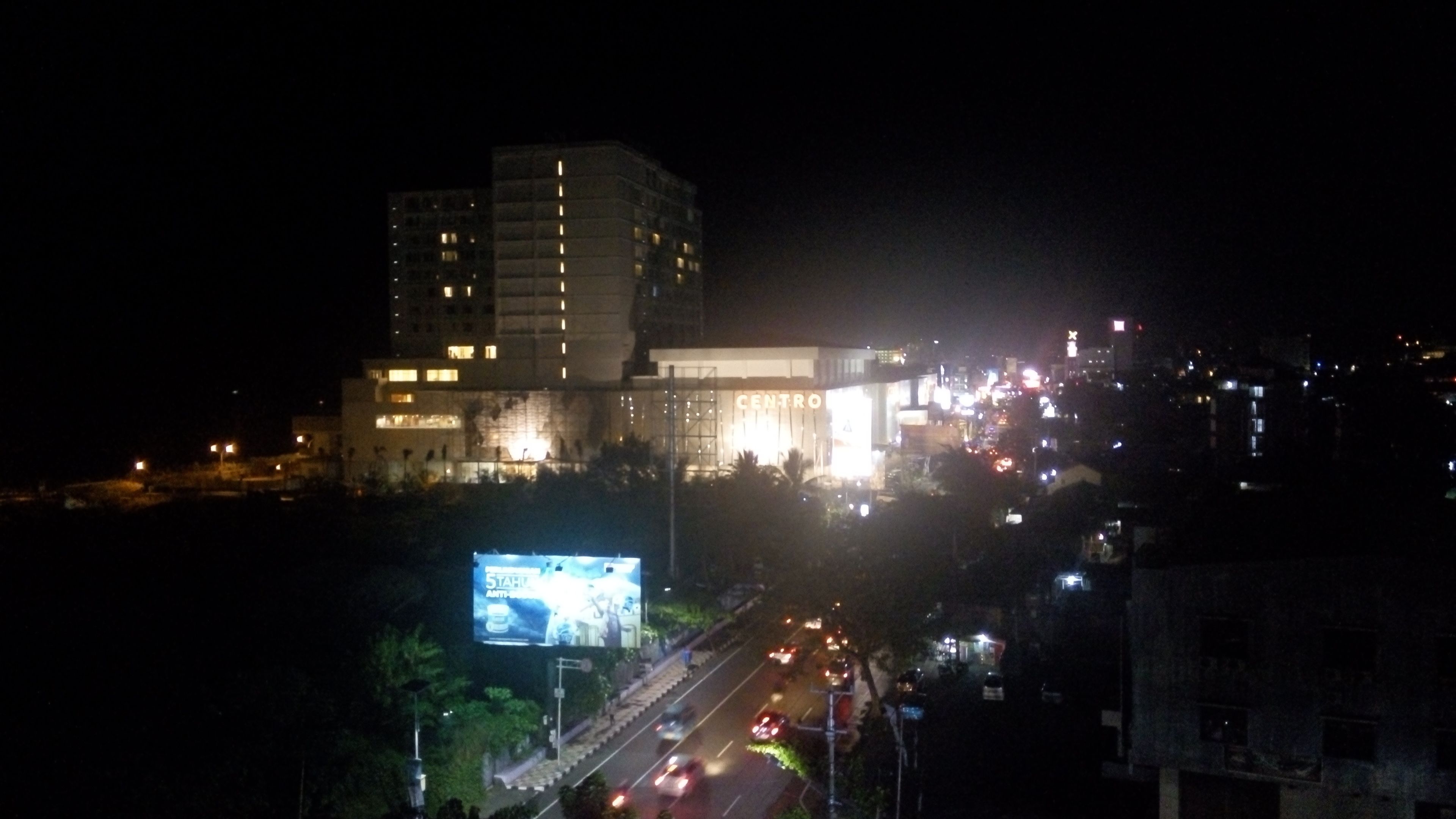 A multi-story building with illuminated signage, a large billboard, and a busy street with vehicles.