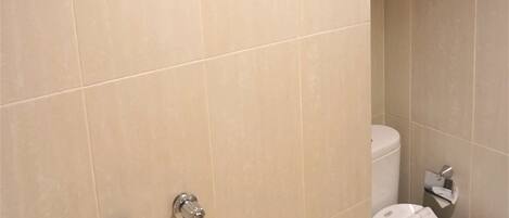 Un baño con azulejos color crema, un inodoro blanco y una ducha con toallero.