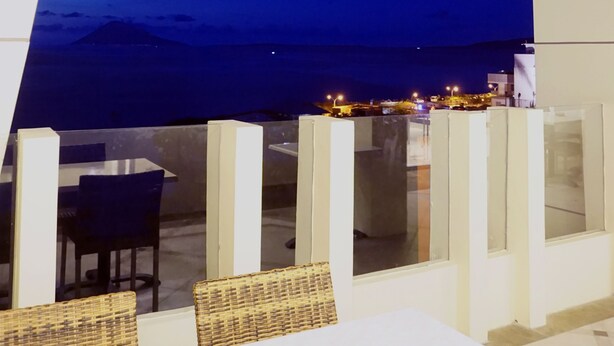 Un área de estar moderna al aire libre con una amplia vista panorámica del cielo nocturno y luces de la ciudad a lo lejos.