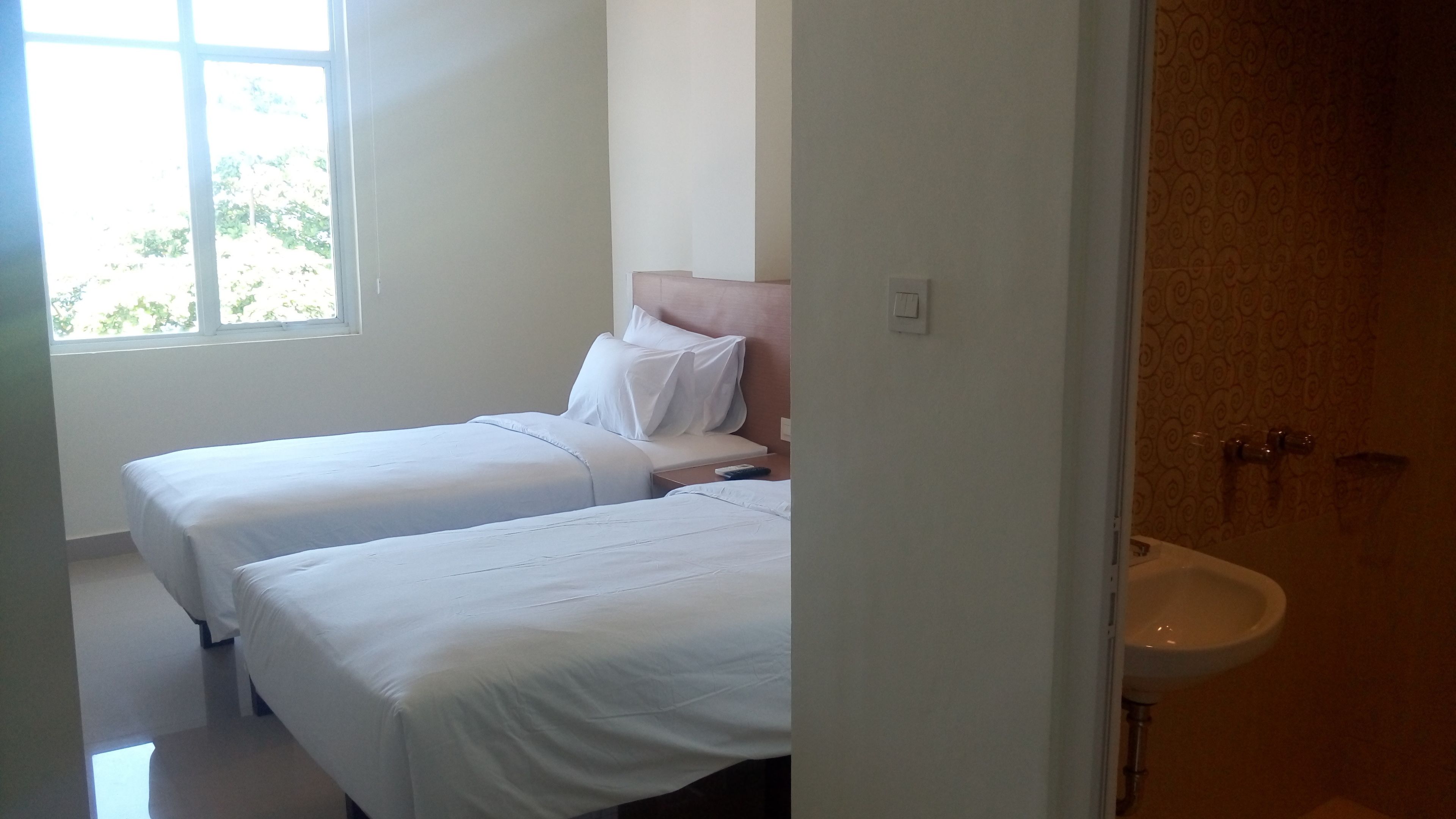 A hotel room with two single beds, a window, and a bathroom with a sink.