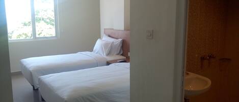 A hotel room with two single beds, a window, and a bathroom with a sink.