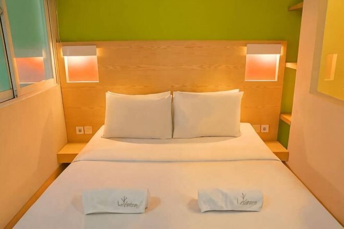 A neatly made bed with white linens and pillows, two towels on the bed, and two bedside lamps on either side.