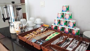 A breakfast buffet setup with coffee, tea, and cereal options, along with utensils and cups. - LeGreen Suite Senayan (Jakarta)