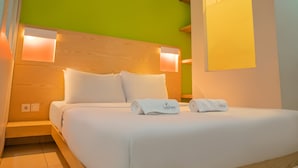 A hotel room with a wooden headboard, white bedding, and two rolled towels with 'LeKreen' branding. - LeGreen Suite Senayan (Jakarta)