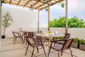 A covered outdoor patio with a round table and chairs, potted plants, and a view of greenery. - LeGreen Suite Poso (Jakarta)