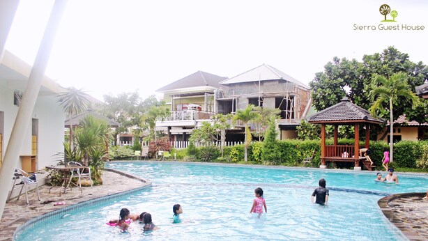 A swimming pool area with multiple people, a gazebo, and a building with a balcony. - Sierra Villa Malang (Malang)