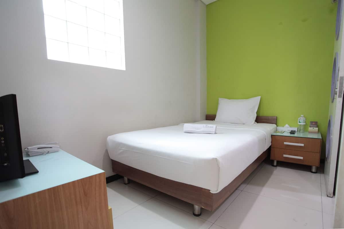 Habitación de hotel con cama, escritorio con teléfono, mesita de noche con lámpara y ventana.