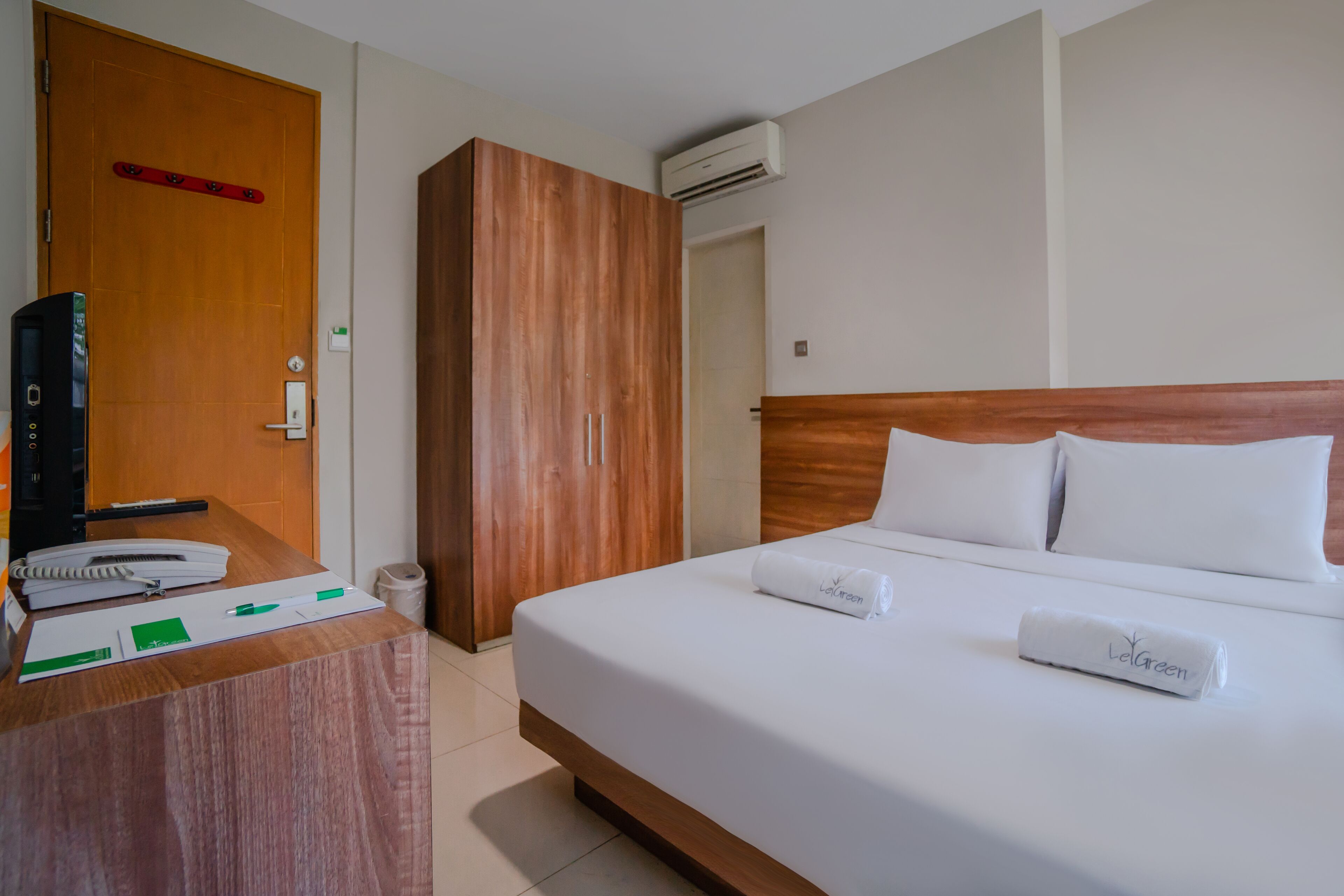 A hotel room with a wooden desk, a bed with white linens, and a wardrobe.