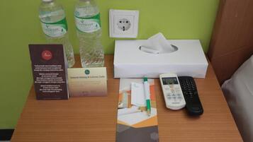 A hotel room with a wooden desk, two bottles of water, a tissue box, a Panasonic remote, a brochure, and a sign.
