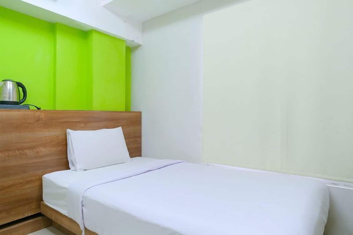 Una cama individual con cabecera de madera, almohada y manta blancos.