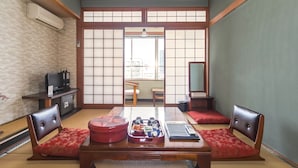 Ett traditionellt japanskt rum med tatamimattor på golvet, ett lågt bord med diverse föremål på och en tv-apparat placerad på ett skåp.