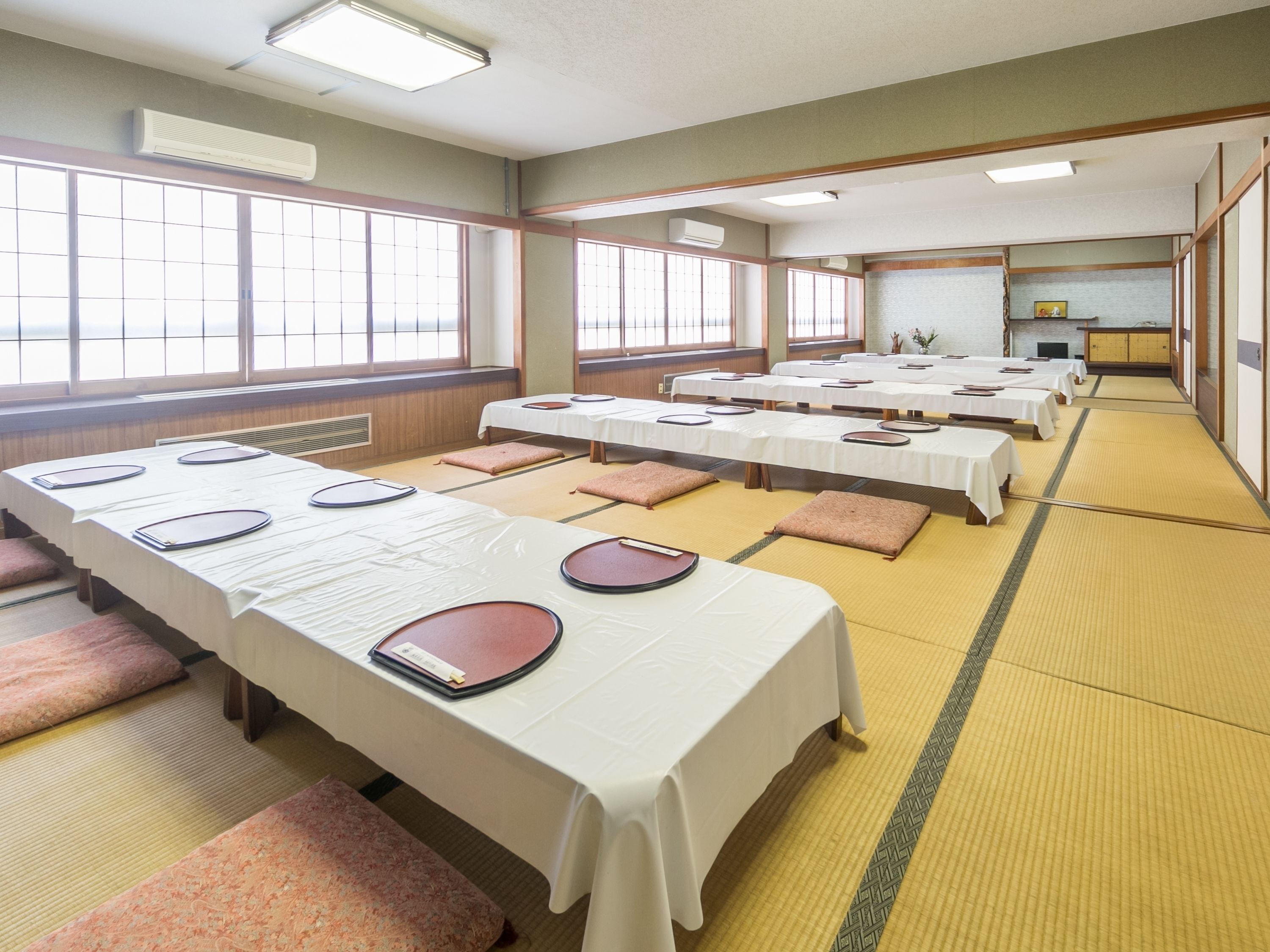 A traditional Japanese-style room with tatami mat flooring, multiple tatami mat seating areas, and tables set for a meal.
