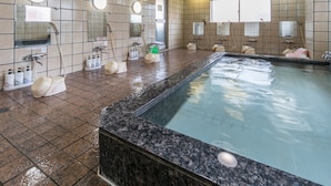 Ett spaområde med ett stort bubbelbad, flera duschmunstycken och ett kaklat golv.