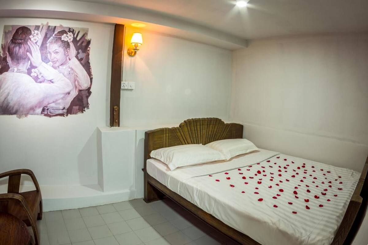 A bedroom with a bed, a wooden headboard, a wall-mounted light, a chair, and a painting.