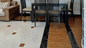 A modern living room with a sofa, dining table, and chairs. There is a wall-mounted light fixture above the table. - Rumnea Apartment (Phnom Penh)
