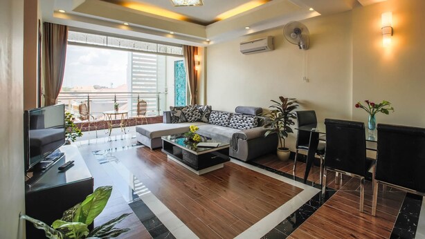 A modern living room with a sofa, coffee table, TV, and dining area. - Rumnea Apartment (Phnom Penh)