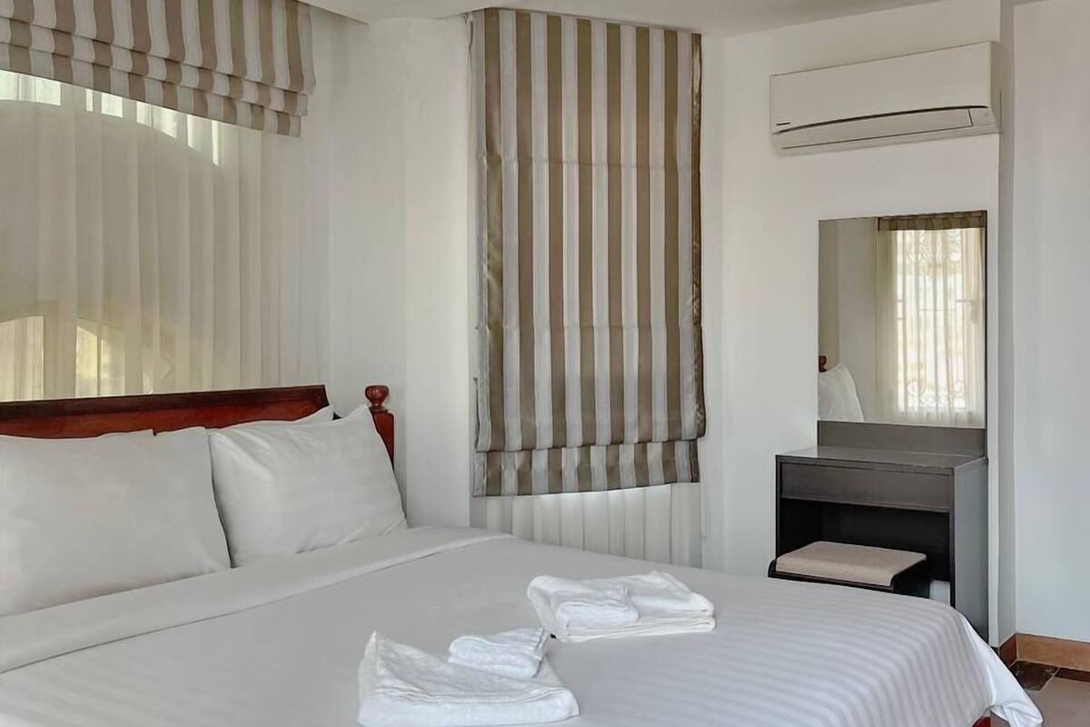 Ein Hotelzimmer mit einem großen Bett, einem Holz-Kopfteil, einem Nachttisch mit Spiegel und einer Klimaanlage an der Wand.