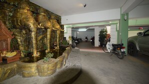 A parking garage with a golden elephant sculpture, a white scooter, and a green car. - Rumnea Apartment (Phnom Penh)