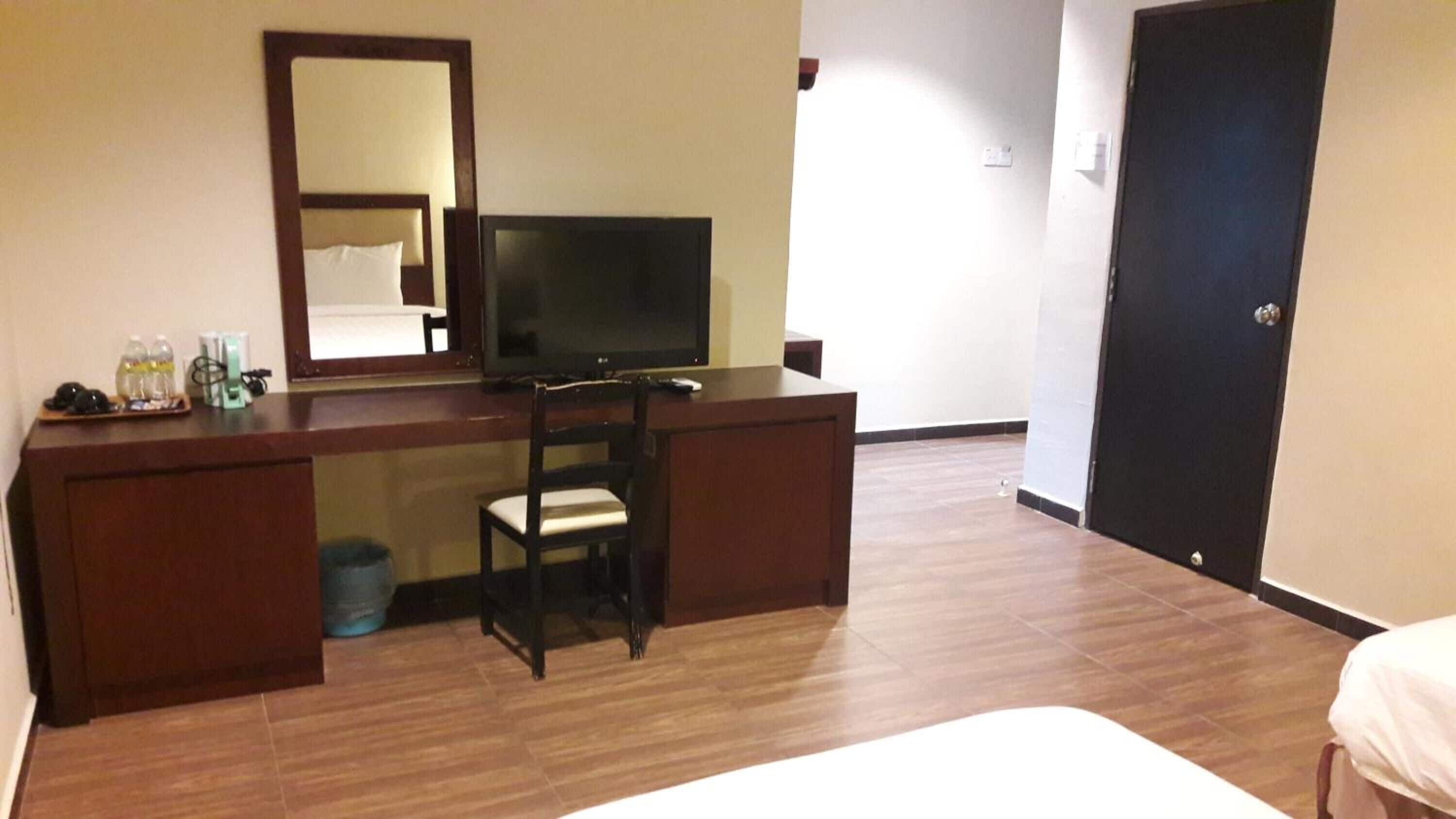 Una camera d'albergo con una scrivania in legno, una televisione, una sedia, un letto e una porta.