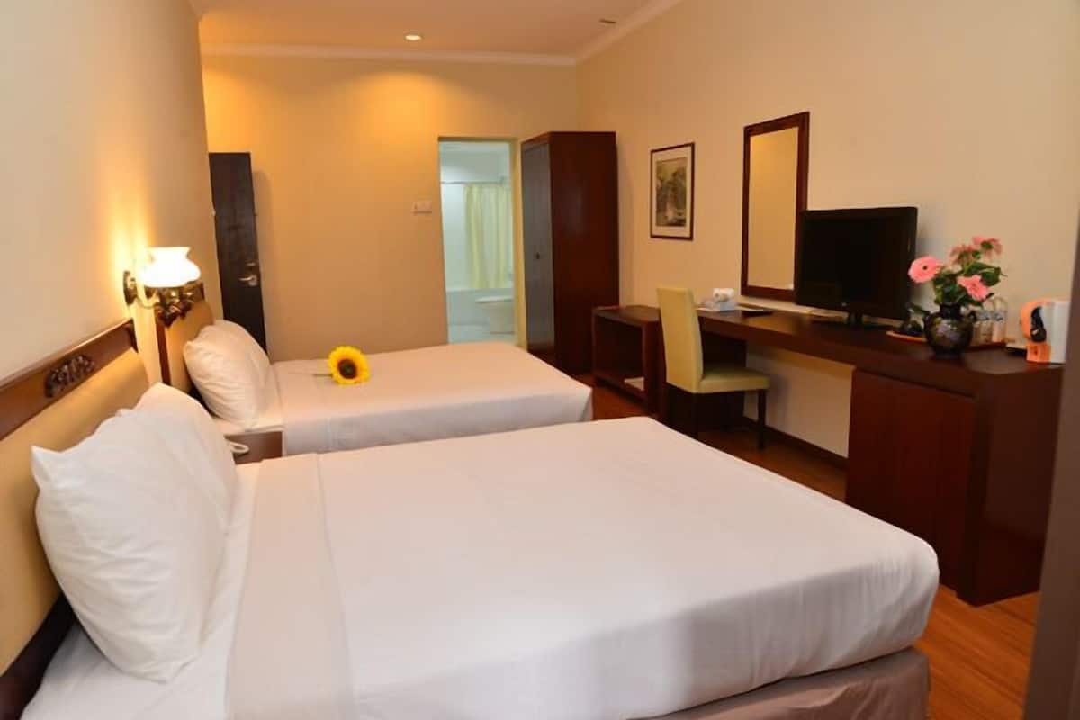 A hotel room with two beds, a desk, a chair, a television, and a vase with flowers.