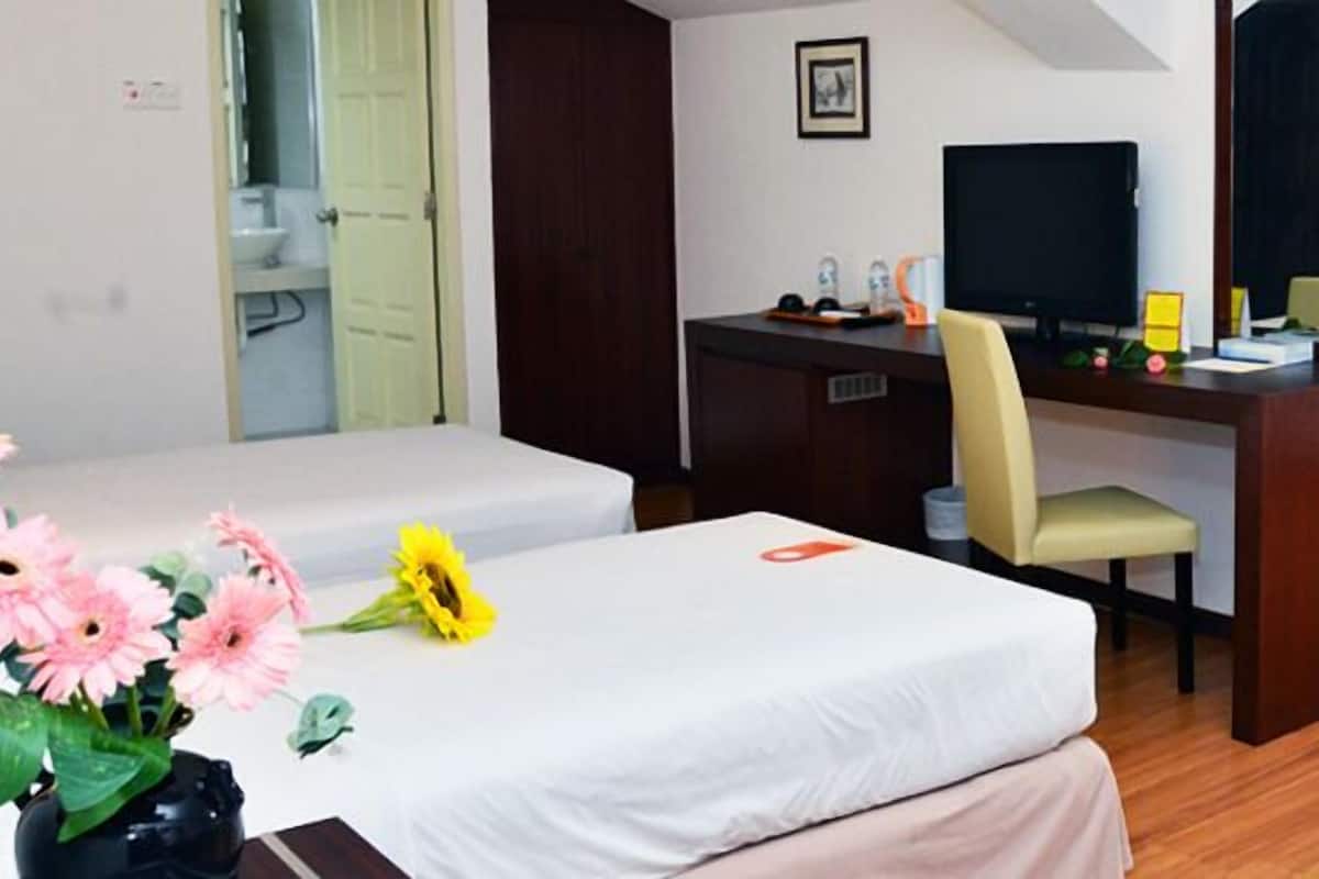 A hotel room with a bed, a desk, a chair, a TV, and a bathroom visible through an open door.