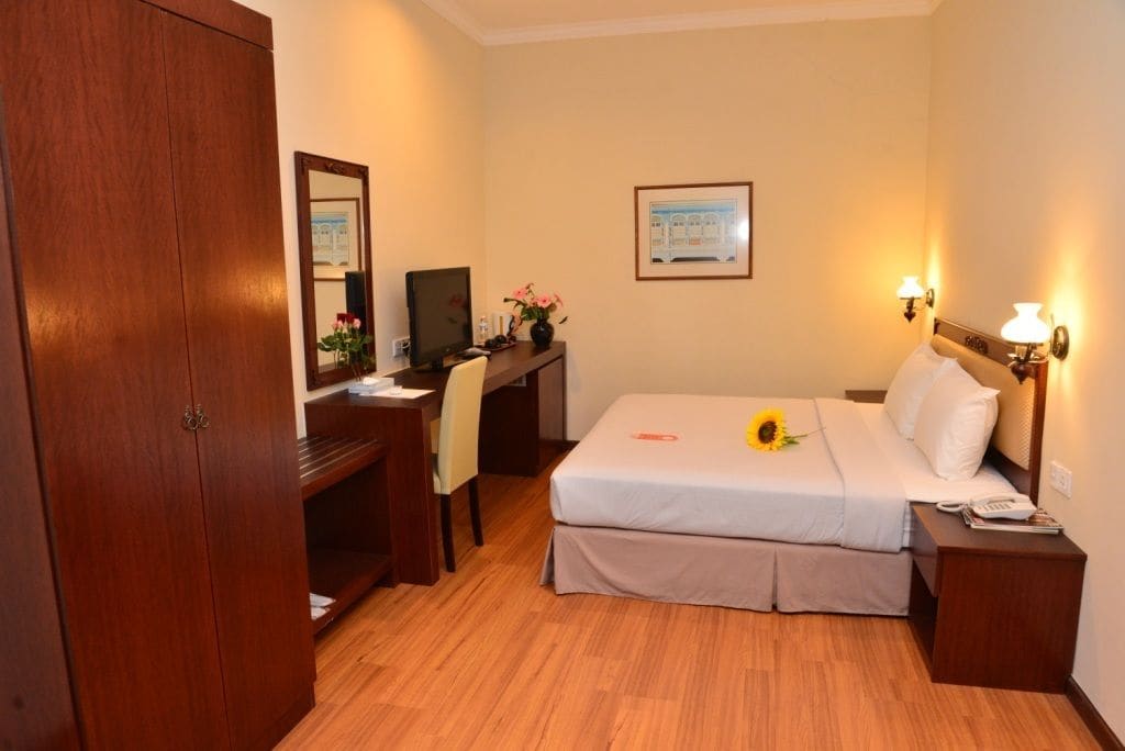 Ein Hotelzimmer mit einem Bett, einem Schreibtisch mit Computer, einem Sessel, einem Holzschrank und einem Nachttisch mit Lampe.