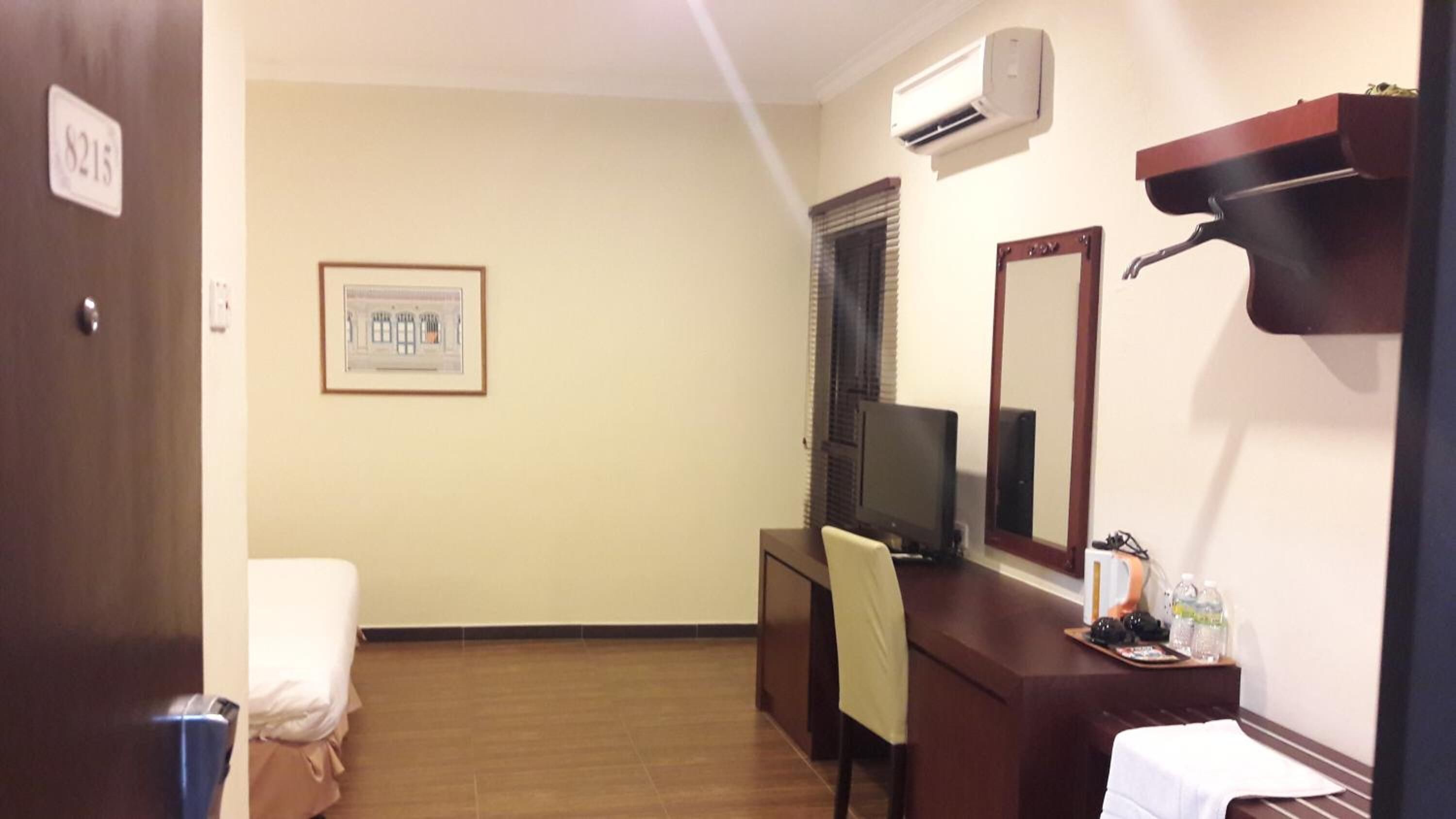 Una habitación de hotel con una cama, un escritorio con una computadora, un espejo y un equipo de aire acondicionado.